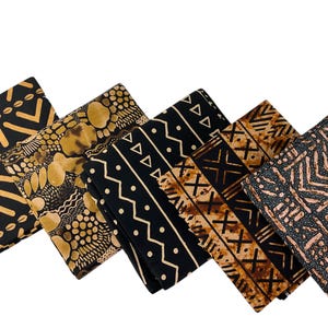 May include: Five folded pieces of fabric arranged in a row, each featuring distinct black and gold or brown geometric patterns. The designs include repeating triangles, dots, chevron lines, and abstract shapes printed on dark textile surfaces.