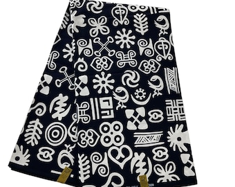 Pode incluir: Uma peça de tecido azul-marinho escuro dobrada com um padrão repetitivo de símbolos Adinkra brancos. O tecido inclui uma pequena etiqueta dourada na borda inferior com o texto impresso: DOUBLE COTTON PRINTS ANTIQUITY WAX 328.