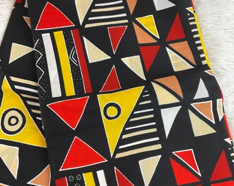 May include: Folded black fabric with a geometric pattern of red, yellow, tan, and white triangles, circles, and stripes. The fabric has a bold, graphic design.