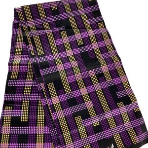 May include: A folded fabric with a repeating pattern of purple, yellow, and black dots and lines. The design creates a plaid-like effect. The fabric is likely used for clothing or home decor.
