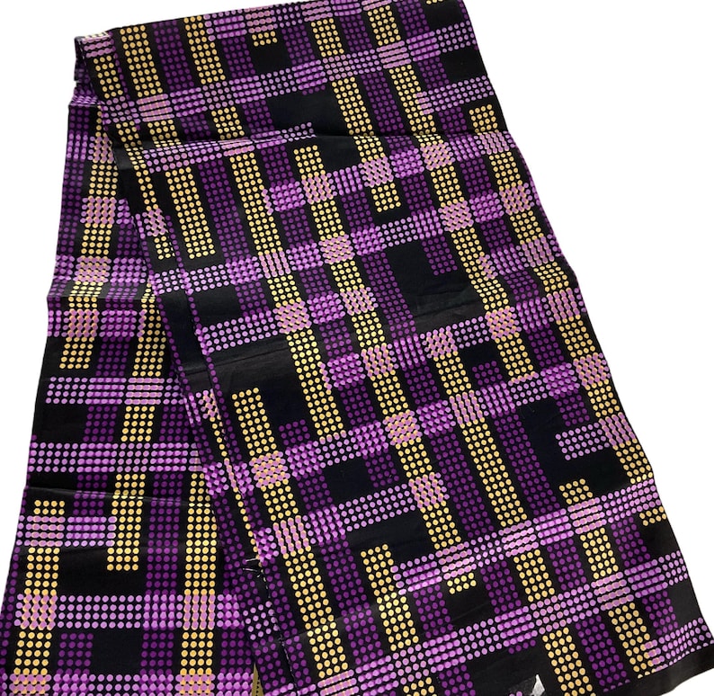 May include: A folded fabric with a repeating pattern of purple, yellow, and black dots and lines. The design creates a plaid-like effect. The fabric is likely used for clothing or home decor.