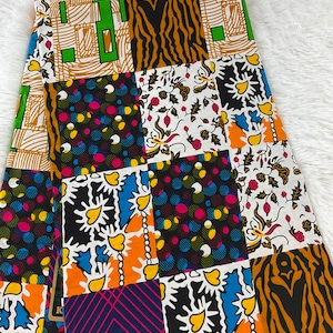 May include: A colorful fabric with a patchwork design. The fabric features a variety of patterns, including stripes, polka dots, and floral designs. The fabric is made up of different colors, including black, white, yellow, orange, blue, green, and pink.