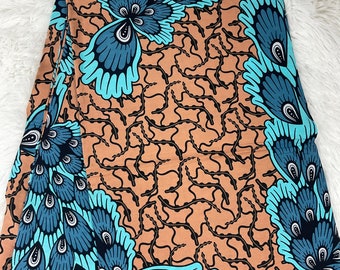 May include: A brown fabric with a repeating pattern of blue and turquoise peacock feathers. The fabric has a subtle texture and a slightly faded look.