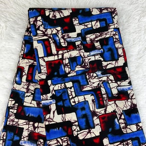 May include: Folded fabric with a bold geometric pattern in blue, red, black, and white. The design features rectangular and angular shapes with a textured, abstract overlay. The fabric is likely cotton or a similar material, suitable for clothing or home decor.