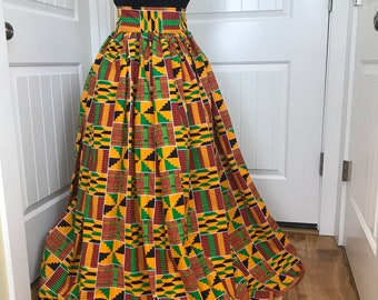 May include: A long, flowing maxi skirt with a high waist and a colorful African print pattern in shades of yellow, green, red, and black. The skirt is pleated and has a wide waistband.