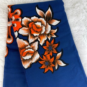 May include: A blue fabric with a white and orange floral pattern. The fabric has a textured surface.