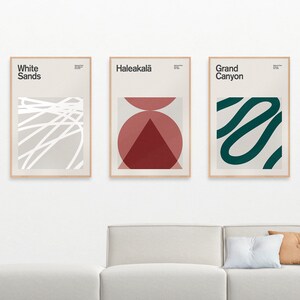 May include: Three framed abstract art prints with minimalist designs. The left print features white lines on a light gray background with the text "White Sands". The middle print features a red and pink geometric design with the text "Haleakala". The right print features a green squiggly line on a light gray background with the text "Grand Canyon".