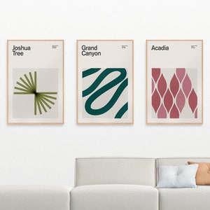 May include: Three framed art prints with minimalist designs. The prints feature the text "Joshua Tree," "Grand Canyon," and "Acadia." Each print has a unique abstract design in shades of green, teal, and red. The frames are a light wood color.