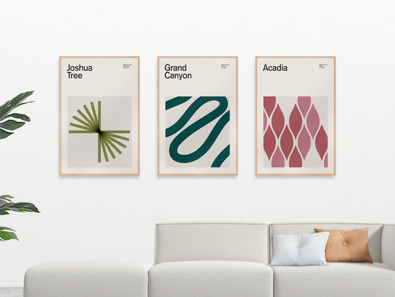 May include: Three framed art prints with minimalist designs. The prints feature the text "Joshua Tree," "Grand Canyon," and "Acadia." Each print has a unique abstract design in shades of green, teal, and red. The frames are a light wood color.