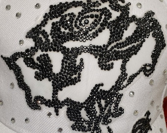 May include: White baseball cap with a black rhinestone rose design. The rose is made of small black rhinestones and has a stem and leaves.