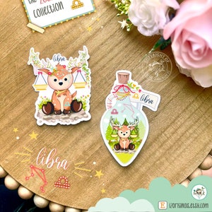 May include: A set of three stickers featuring a cute deer with a Libra zodiac symbol. The stickers are on a wooden surface with a light blue background. The stickers are part of a collection called "The Zodiac Collection, Part 9".