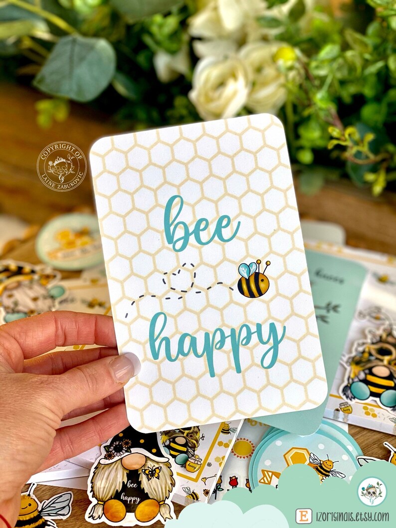 May include: A white card with a honeycomb pattern and the text "bee happy" in blue. A cartoon bee with black and yellow stripes is flying above the text.