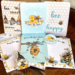May include: A set of bee-themed stationery featuring gnomes, bees, and honeycomb designs. The stationery includes notepads, stickers, and a small round sticker with the text "save the bees".