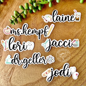 K&ouml;nnte beinhalten: Ein Set mit 6 personalisierten Namenaufklebern mit verschiedenen Symbolen, die verschiedene Berufe repr&auml;sentieren. Die Namen sind "ms. kempf", "lori", "jacci", "dr. geller", "jodi" und "laine".