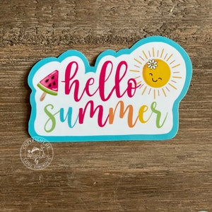 以下が含まれることがあります： 青い縁取りと「hello summer」の文字がピンク、オレンジ、緑色で書かれたカラフルなステッカー。ひまわりとスイカの棒アイスを持った笑顔の太陽が特徴です。