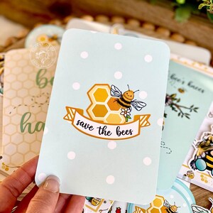 May include: A light blue card with white polka dots features a cartoon bee with a honeycomb and a banner that reads "save the bees".