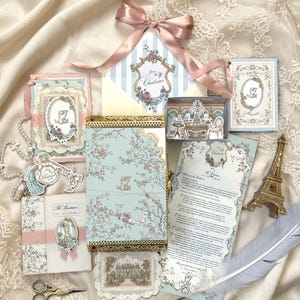 May include: A collection of stationery featuring a light blue box with floral patterns, an envelope with a pink ribbon, a miniature Eiffel Tower, a feather quill, and small scissors. The items include cards with ornate frames, text reading The Invitation, and illustrations of a chateau and interior scenes.