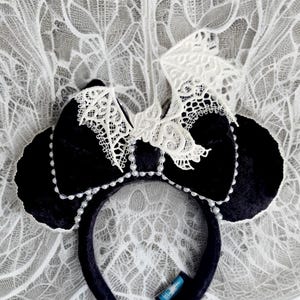 May include: Black velvet Minnie Mouse ears with a white lace bow and pearl accents. The bow is shaped like a bat.