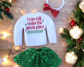 May include: White elf-sized sweater with the text "I can still make the whole place shimmer" in red and green embroidery. Green sequin skirt with a white headband and red bow.