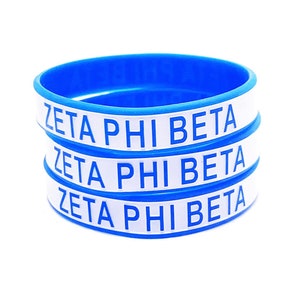 Puede incluir: Tres pulseras de silicona azul con letras blancas que dicen "Zeta Phi Beta" en cada una.