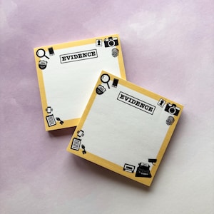 Puede incluir: Dos blocs de notas adhesivas amarillas con bordes negros e iconos. Los blocs tienen la palabra "EVIDENCE" impresa.