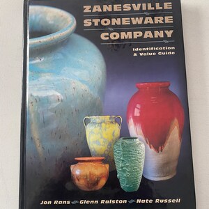 May include: A book titled "ZANESVILLE STONEWARE COMPANY Identification & Value Guide" by Jon Rans, Glenn Ralston, and Nate Russell. The cover features a collection of colorful ceramic pottery.