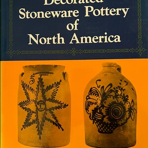 May include: A book titled "Decorated Stoneware Pottery of North America" by Donald Blake Webster. The cover features two antique stoneware jugs with black painted designs on a tan background.
