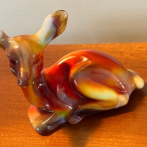 May include: A glass deer figurine with a swirled pattern in shades of red, orange, and yellow.