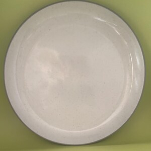 May include: A round, off-white ceramic plate with a speckled surface and a gray rim. The plate is a simple, minimalist design, suitable for serving food. The plate is a neutral color, making it versatile for various table settings.
