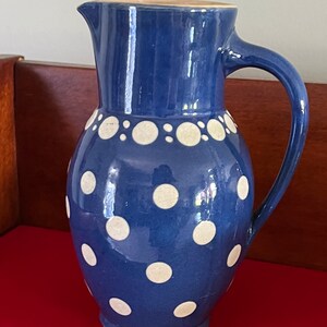 May include: A blue ceramic pitcher with white polka dots. The pitcher has a handle and a spout.