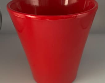 May include: A glossy, bright red ceramic vase with a flared, conical shape. The vase has a smooth, polished surface and a wide opening. The design is simple and modern, suitable for displaying flowers or as a decorative accent.