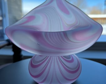 May include: A pink and white swirl glass bowl with a wide, shallow base and a tall, pointed top. The bowl is made of clear glass with pink and white swirls throughout.