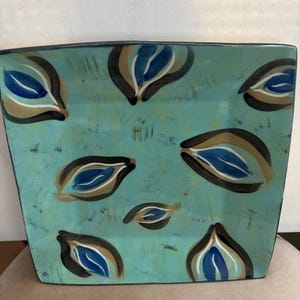 May include: A square ceramic serving platter with a teal blue background and a pattern of stylized blue, brown, and white leaves.