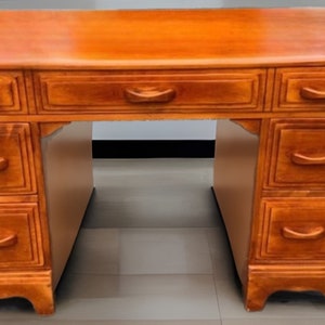 May include: A wooden desk with a warm, honey-toned finish. It features multiple drawers with curved handles and a spacious work surface. The desk has a classic design, suitable for a home office or study.