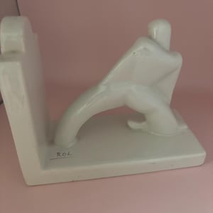 May include: White ceramic bookends shaped like a stylized human figure. The bookends are signed "ROL" on the base.