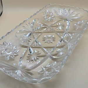 May include: A clear glass serving dish with a starburst pattern. The dish has a scalloped edge and is perfect for serving snacks or desserts.