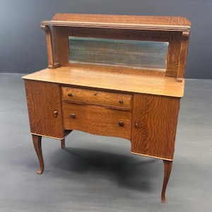 May include: A vintage wooden sideboard with a mirrored back and two doors. The sideboard has a curved front and sits on four legs.
