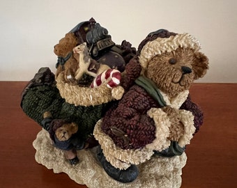 Könnte beinhalten: Eine Weihnachtsfigur aus braunem Stofftier, das einen rot-weißen Weihnachtsmann-Hut trägt und einen Sack mit Geschenken trägt. Der Bär steht auf einem schneebedeckten Sockel mit einer kleineren braunen Stofftierfigur daneben.