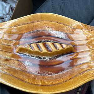 May include: A brown and gold ceramic dish with a wavy design and a raised, ribbed handle in the center. The dish has a glossy finish.