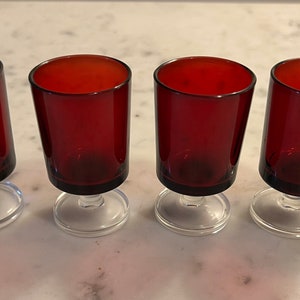 May include: Set of four red glass shot glasses with clear stems and bases.