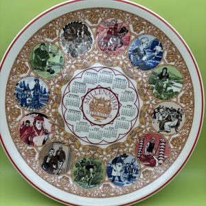 May include: A white ceramic plate with a red rim features a calendar for the year 1999 and illustrations of famous authors and their works. The plate is decorated with gold trim and features the text "Millennium Literature 1999".