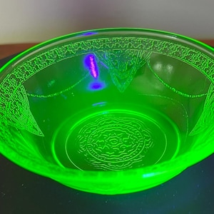 Könnte beinhalten: Eine grüne Glasschüssel mit einem dekorativen, geätzten Design. Die Schüssel ist aus Uran-Glas, das unter Schwarzlicht leuchtet.