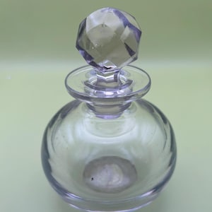 May include: A clear glass bottle with a faceted glass stopper. The bottle has a round body and a short neck.