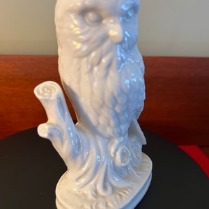 May include: White porcelain owl figurine perched on a tree branch. The owl has detailed feathers and a realistic appearance.