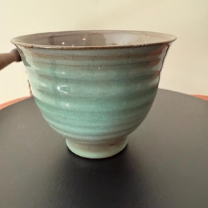May include: A green and brown ceramic bowl with a wavy design. The bowl is sitting on a black surface.