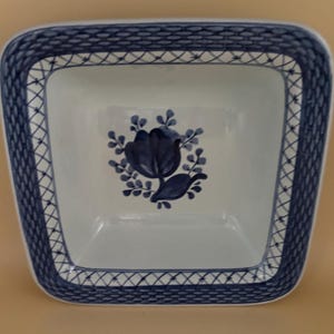 May include: A white square ceramic serving dish with a blue and white floral design. The dish has a woven border design.