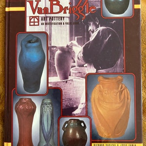Op de afbeelding: De omslag van het boek The Collector's Encyclopedia of Van Briggle Art Pottery: An Identification & Value Guide met een foto van een pottenbakker die aan een pottenbakkerswiel werkt en verschillende voorbeelden van Van Briggle-keramiek, waaronder een blauwe vaas, een bruine vaas, een bruine en oranje vaas en een bruine en oranje vaas met handvatten.
