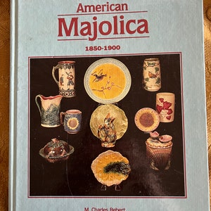 May include: A book titled "American Majolica 1850-1900" by M. Charles Robert. The cover features a colorful illustration of various majolica pieces, including pitchers, mugs, plates, and a butter dish.