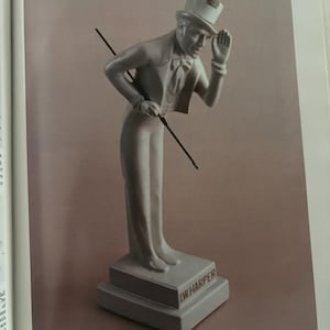 May include: A gray ceramic figurine of a man in a top hat and suit, holding a cane and tipping his hat. The base reads "I.W. HARPER". The figurine is a decanter, a striking example of American pottery.