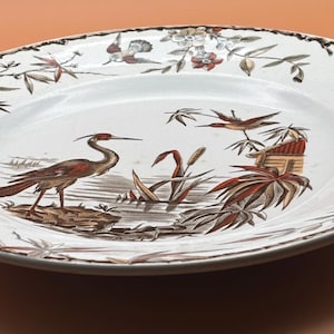 Può includere: Piatto ovale in ceramica con un design dettagliato di uccelli e paesaggi. Il piatto bianco presenta un'illustrazione marrone e rossa di un airone, uccelli e fogliame. Il bordo ha un bordo marrone.